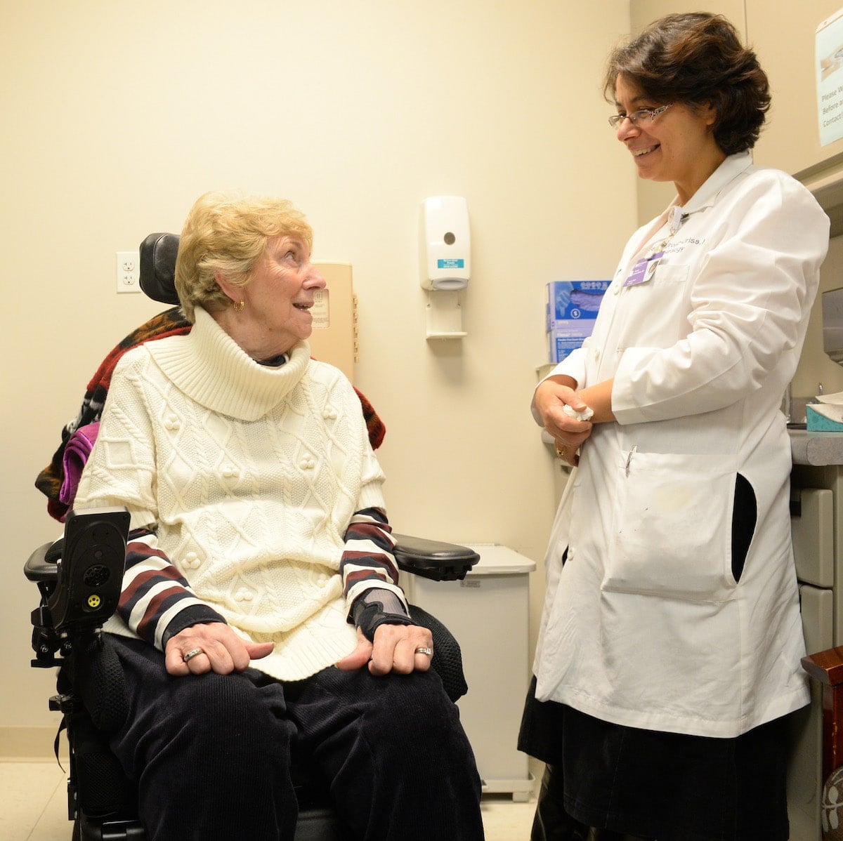 A woman using a power wheelchair talks with her doctor.