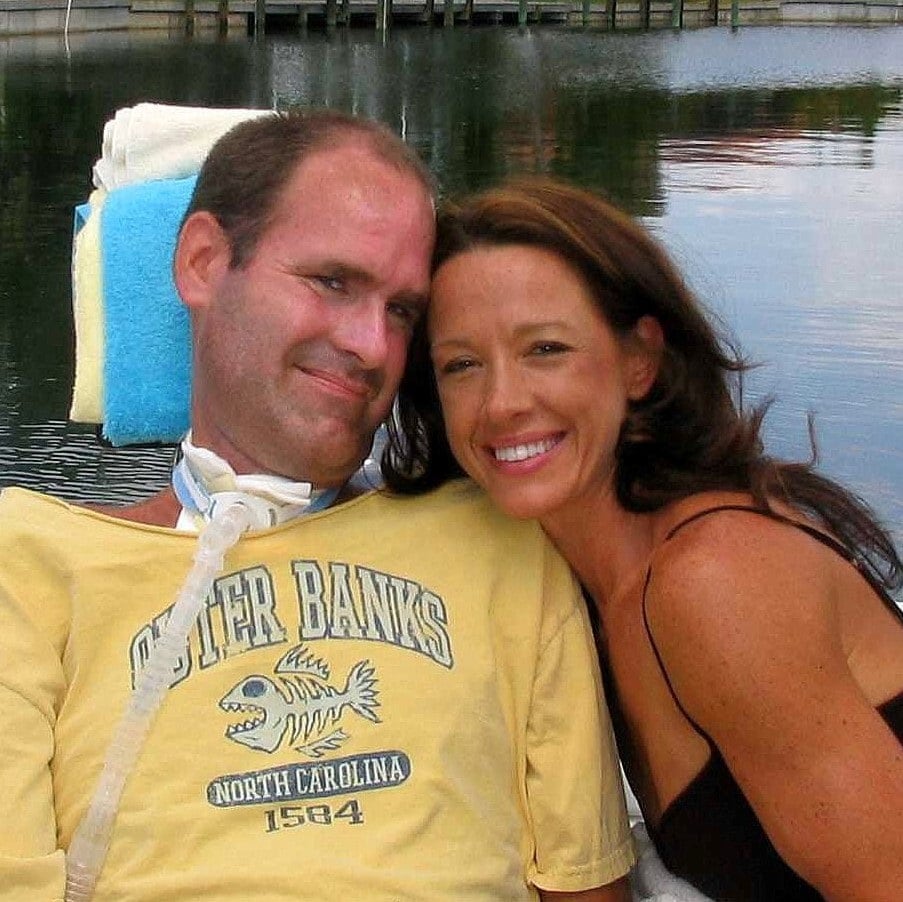 A man with a breathing tube smiles with a loved one.